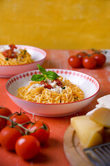 Top view of plates with pasta on red wooden table, surrounded by cheese and tomatoes. Traditional Italian food, rustic homemade meal.
