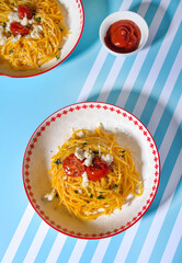 Yellow pasta served on plates on blue background with hard light. Minimal, modern food styling with...