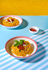 Yellow pasta served on plates on blue background with hard light. Minimal, modern food styling with bright shadows.