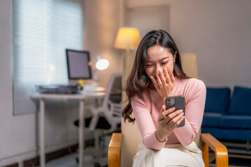 Fototapeta premium woman is sitting in a chair and laughing while looking at her cell phone