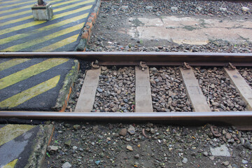 Kertosono, Indonesia July, 06 2025: Close-up view of railway tracks with rocks and a yellow-striped...