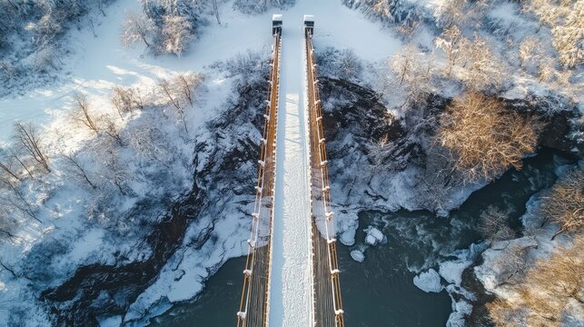 Aerial view of a wooden suspension bridge over a river in a snowy landscape.
