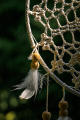 Dreamcatcher with White Feathers Swaying Outdoors Against Blue Sky and Green Trees