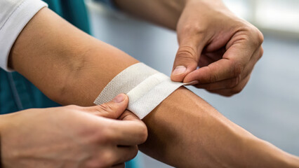 Person applies bandage to arm, demonstrating care and attention to minor injury. This preventive measure is essential for effective wound healing