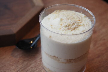 Creamy dessert in a clear cup on wooden table with spoon