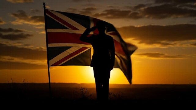 Silhouette of soldier saluting next to waving union jack flag during vibrant golden sunset over