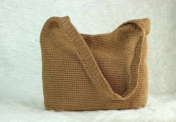Crocheted handmade milky brown bag on furry white blanket.