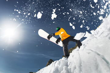 Bottom view of a snowboarder holding a snowboard in his hands and throwing fresh snow into the air...