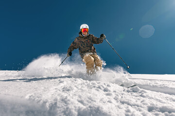 Front view of a skier skiing off-piste in deep snow and raising a cloud of snow behind him, bottom...