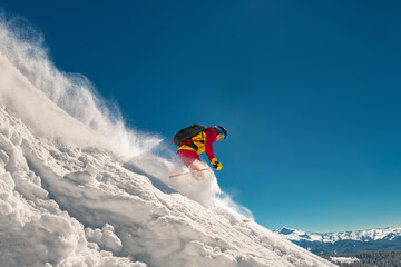 A skier quickly descends a steep slope against a blue sky. Extreme off-piste skiing high in the...