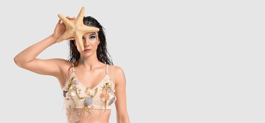 Beautiful young woman dressed as mythical siren with starfish on light background with space for...