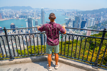 Tourist standing behind and holds onto the fence with his hands on viewpoint observation deck in Hong Kong.