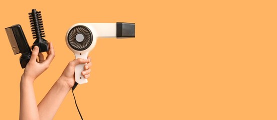 Hands with hair dryer and attachments on orange background with space for text