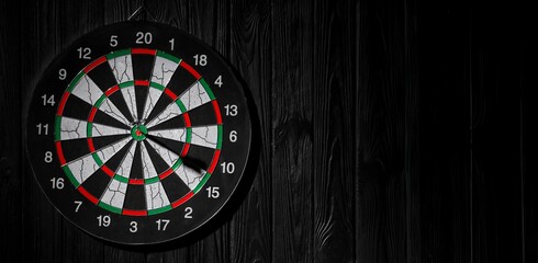 Dartboard with hit bullseye hanging on black wall. Banner for design