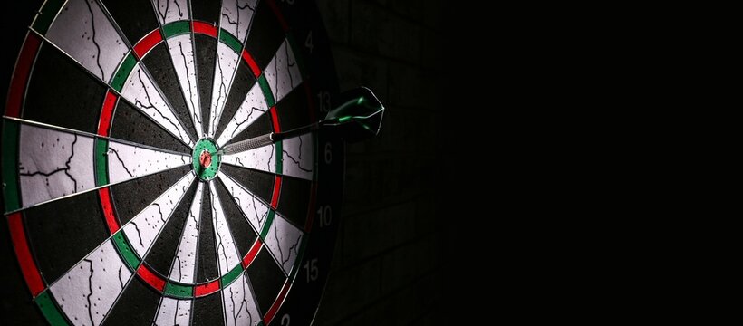 Dartboard with hit bullseye hanging on black wall, closeup. Banner for design
