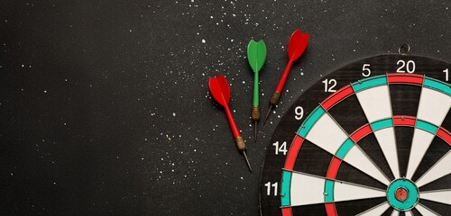 Darts and dartboard on black background with space for text, top view