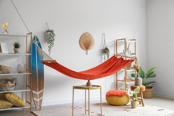 Interior of light living room with cozy red hammock, surfing board and shelving units