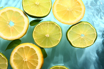 Slices of fresh lemon and lime in water on blue background