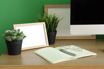 Blank frame with artificial plants and notebook on table in office