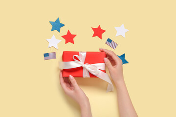 Woman holding gift box with USA flags and stars on pale yellow background. American Independence Day