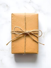 Wrapped gift box in brown paper with twine bow on white marble background top view present
