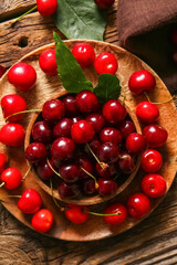 Plate and bowl with sweet cherries on wooden background