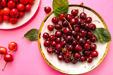 Plates with sweet cherries and leaves on pink background
