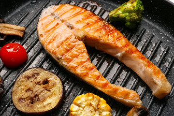 Tasty grilled salmon steak with vegetables in frying pan, closeup