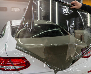 Applying tinting foil on a car window in the tuning studio. Male car service worker glue window...