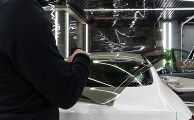 Applying tinting foil on a car window in the tuning studio. Male car service worker glue window...
