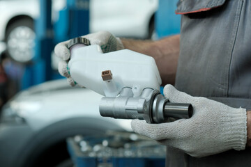 Car service center.The car mechanic holds the main brake cylinder with a reservoir in his hands....