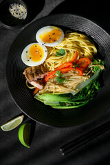 Top view of ramen in black bowl. Traditional Japanese noodle soup with rich broth, vegetables, and toppings.