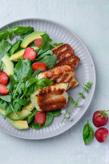 Plate of summer salad with fresh strawberries, arugula, and grilled halloumi cheese. Bright,...