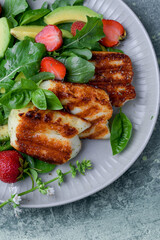 Plate of summer salad with fresh strawberries, arugula, and grilled halloumi cheese. Bright, flavorful, and healthy dish perfect for warm seasons.