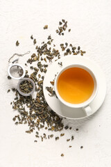 Cup of tea with infuser and dry green tea leaves on white textured background