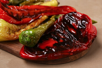 Wooden board with different grilled peppers on brown background