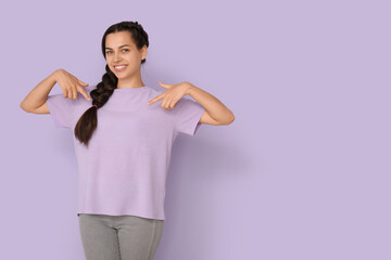 Young woman pointing at her t-shirt on lilac background