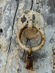 A rusty metal ring is hanging from a wooden door