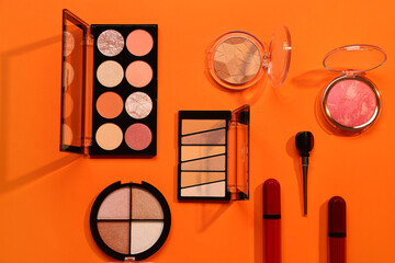 Beautiful palettes of eyeshadows and different decorative cosmetics on orange background