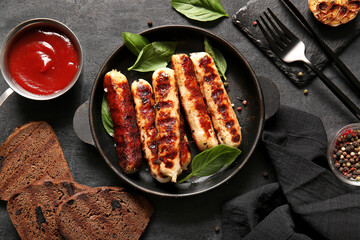 Frying pan of tasty grilled sausages, bread and sauce on black background