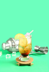 Glass of tasty Long Island iced tea, ice cubes and bartender tools on color background