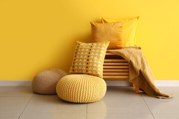 Wooden table with soft cushions near yellow wall