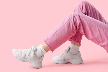 Legs of young woman in stylish white sneakers on pink background