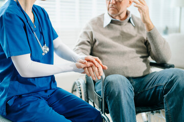A compassionate nurse in blue scrubs holds the hand of a senior patient in a hospital clinic,...