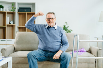 A senior man flexes his arms in celebration of rehabilitation success at home, showcasing strength,...