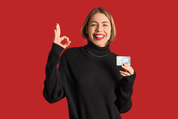 Young woman with credit card showing OK on red background