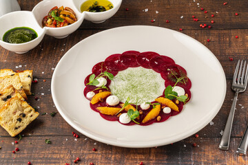 Beet carpaccio with orange slices, fresh greens and cream dots