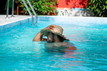 Local Costa Rican man enjoying his vacation in a swimming pool with a straw umbrella in Tortuguero, Costa Rica