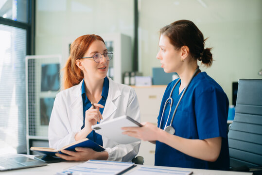 Doctor and nurse team using tablet to review medical results. Diverse healthcare professionals in modern hospital clinic