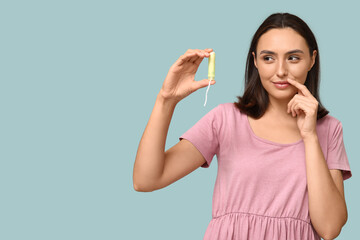 Beautiful thoughtful woman with tampon on blue background